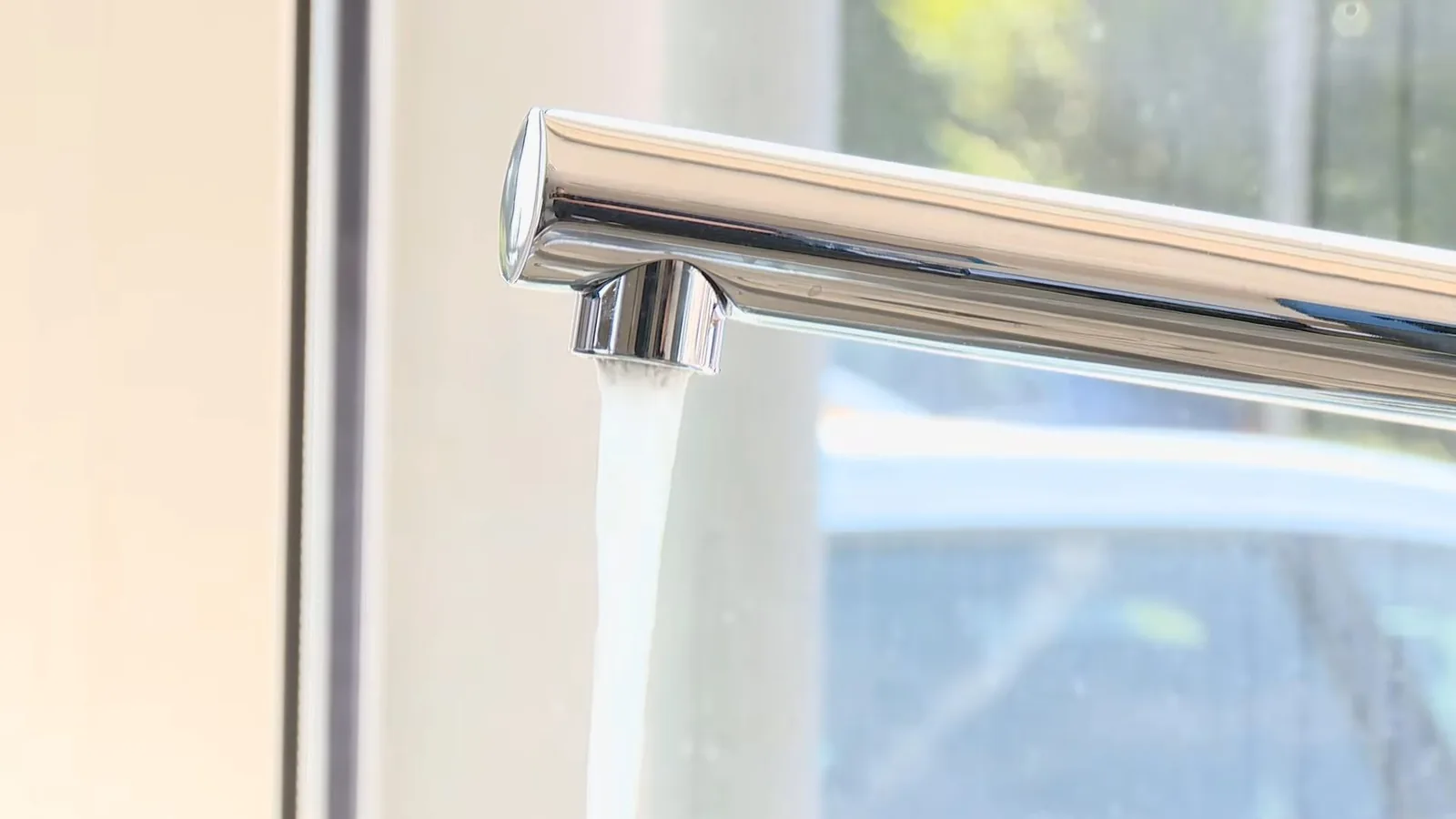 Chrome kitchen faucet running a steady stream of water beside a sunlit window