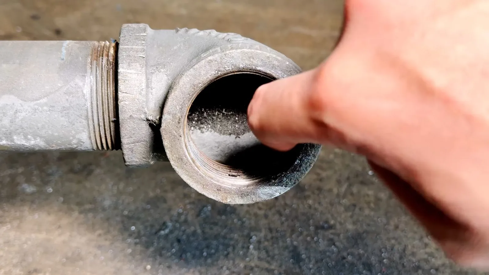 Fingertip inside the open threaded end of an old cast-iron cleanout fitting, with a rough concrete floor behind