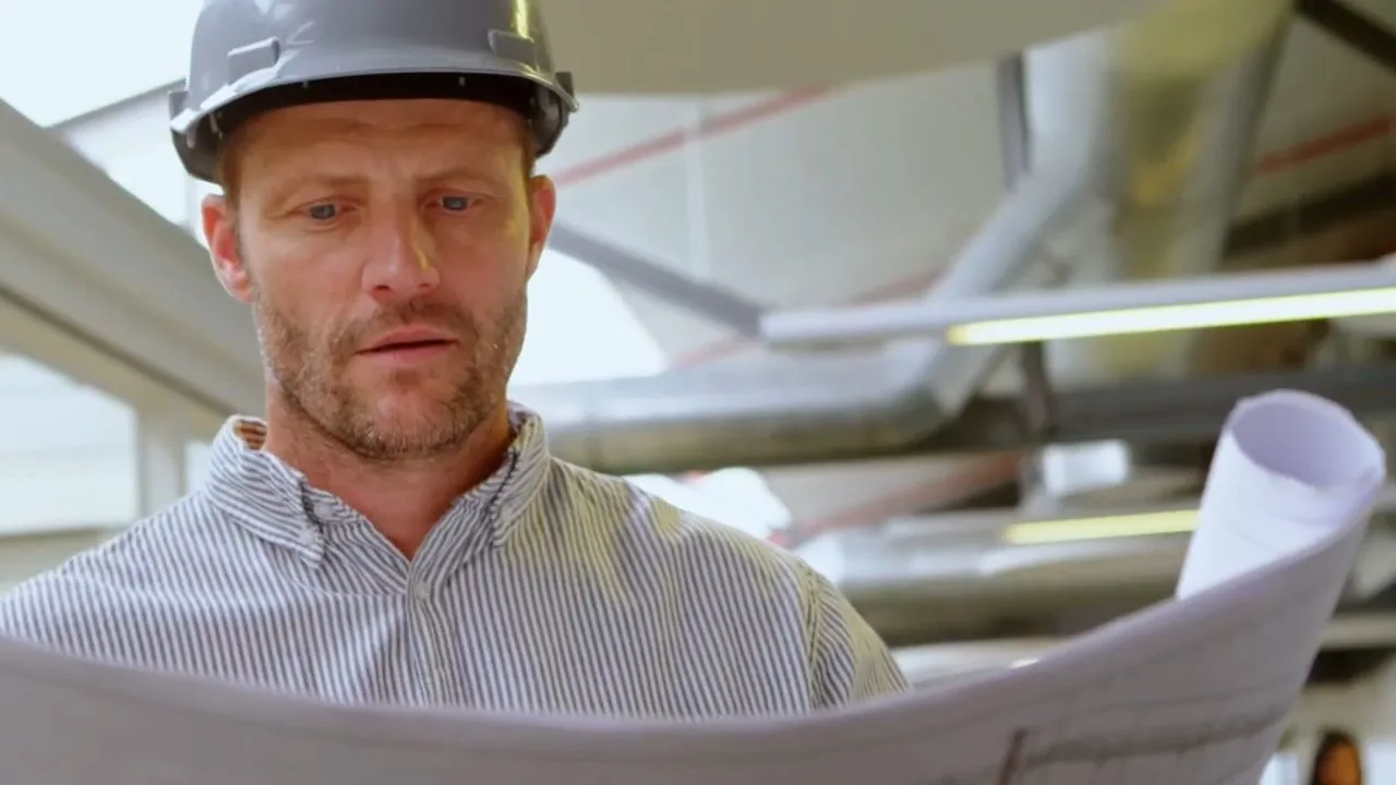 Contractor in a hard hat and striped shirt studying a set of rolled plans