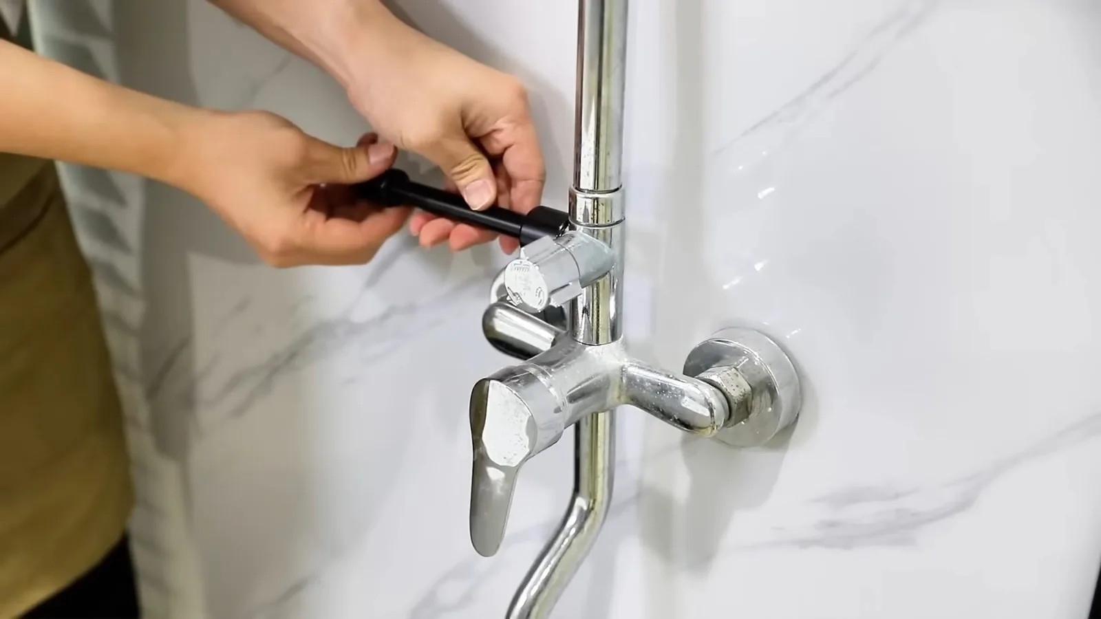 Hands tightening a chrome wall-mounted faucet and spout against a white marble wall