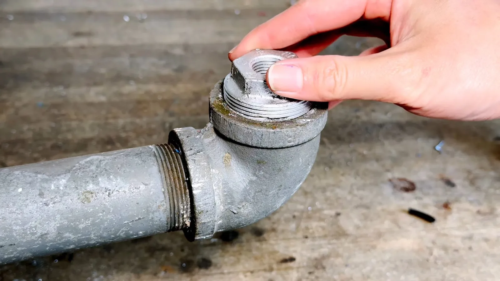 Hand turning the threaded cap on a galvanized cast-iron cleanout fitting at the end of a pipe
