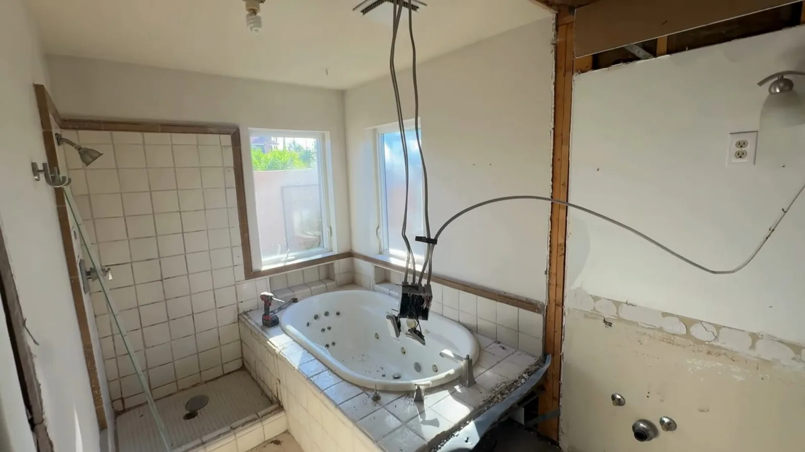 Bathroom with wall coverings removed, a corner tub and a tiled shower, with a window letting in daylight