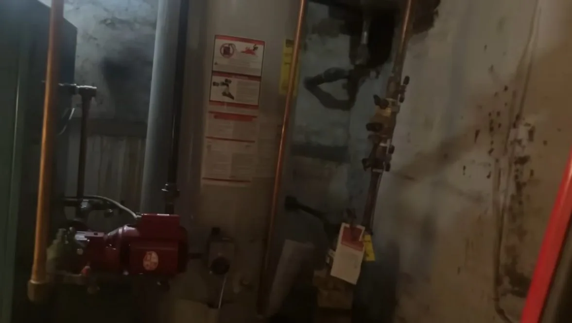 Dim utility room with a red-painted boiler pump, copper pipes and a hanging tag on a valve