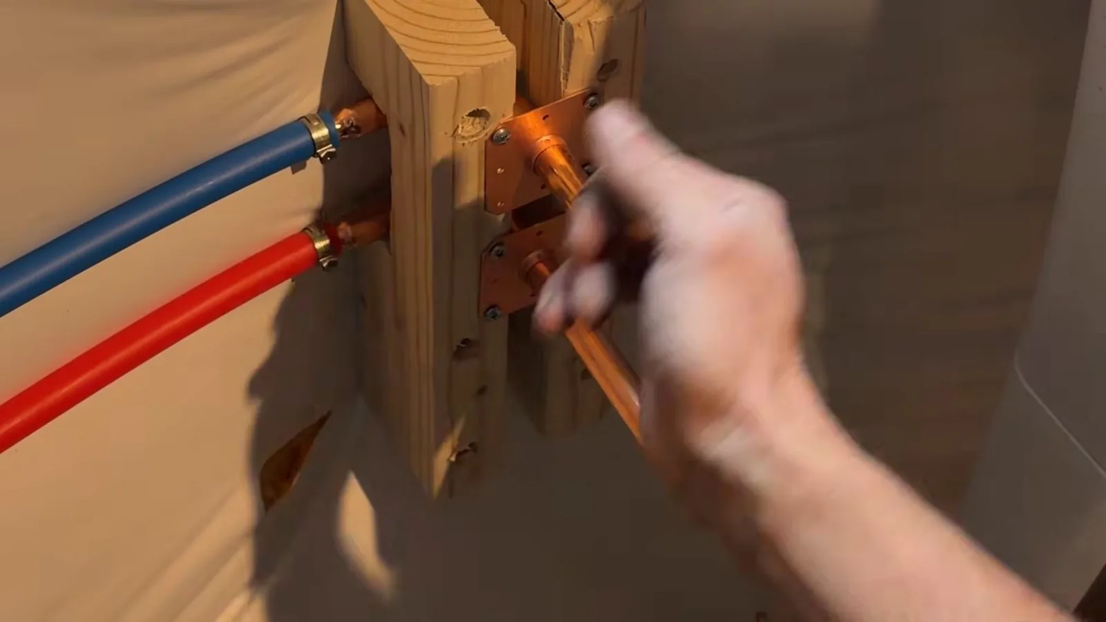 Hand placing a copper fitting at red and blue PEX tubing stub-outs mounted on a wood block