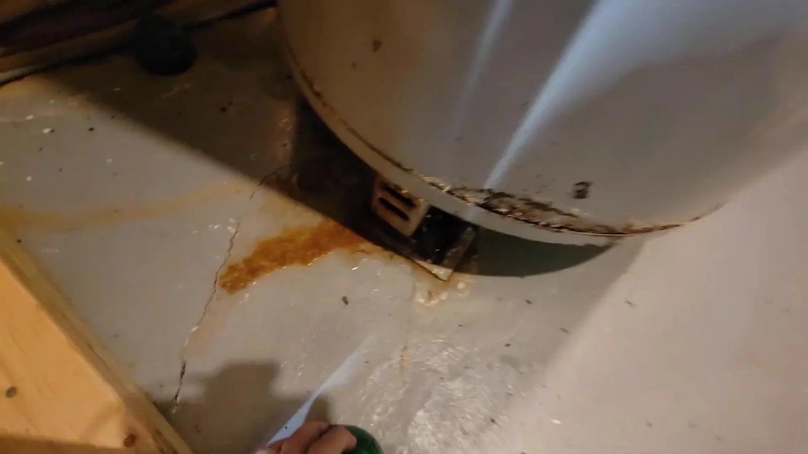Rust-colored stain on a gray concrete floor beside the base of a white tank water heater, with a crack in the slab nearby