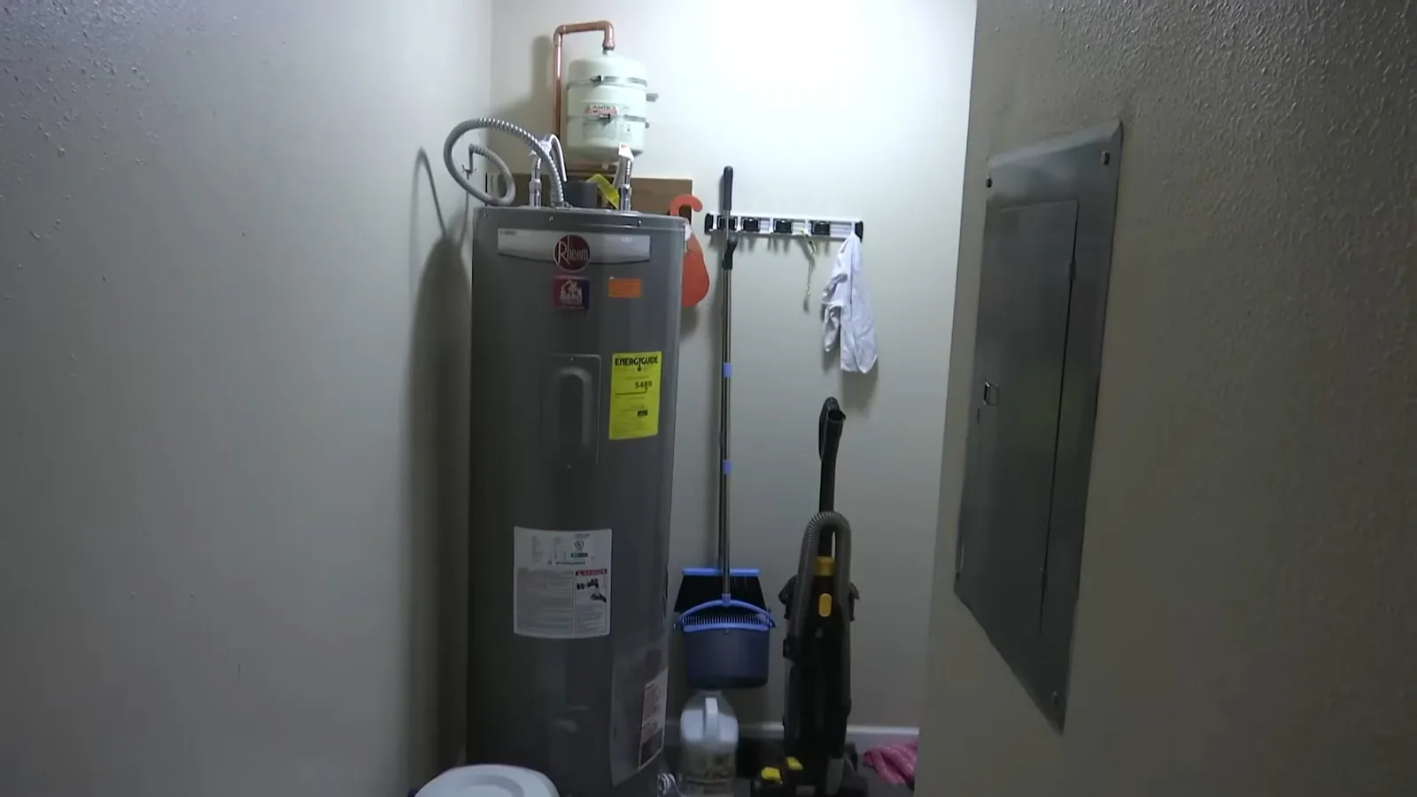 Tank water heater with a small expansion tank on top, standing in a utility closet next to an electrical panel