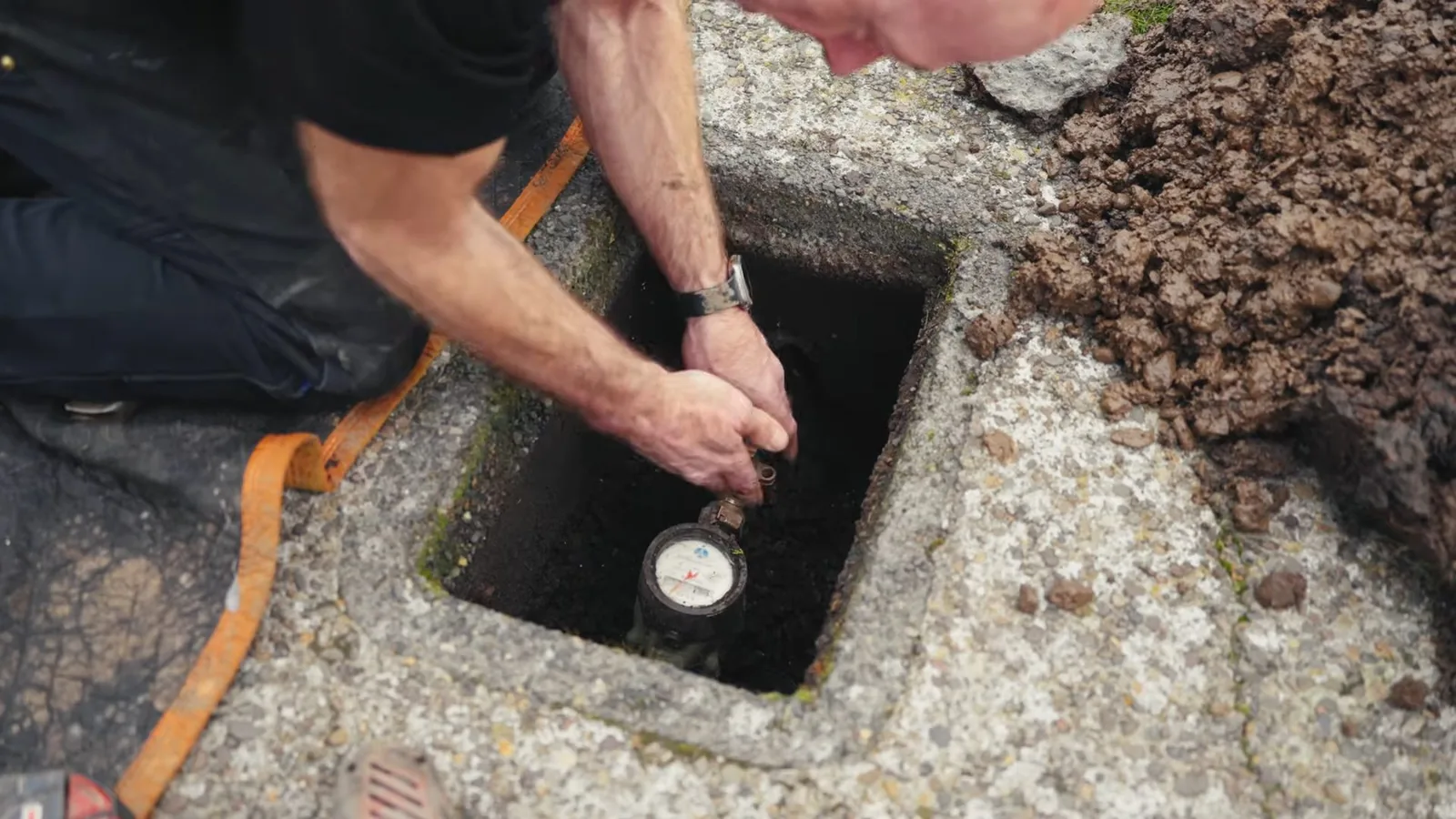 Technician kneeling at a sidewalk meter box and reaching down to the meter dial below