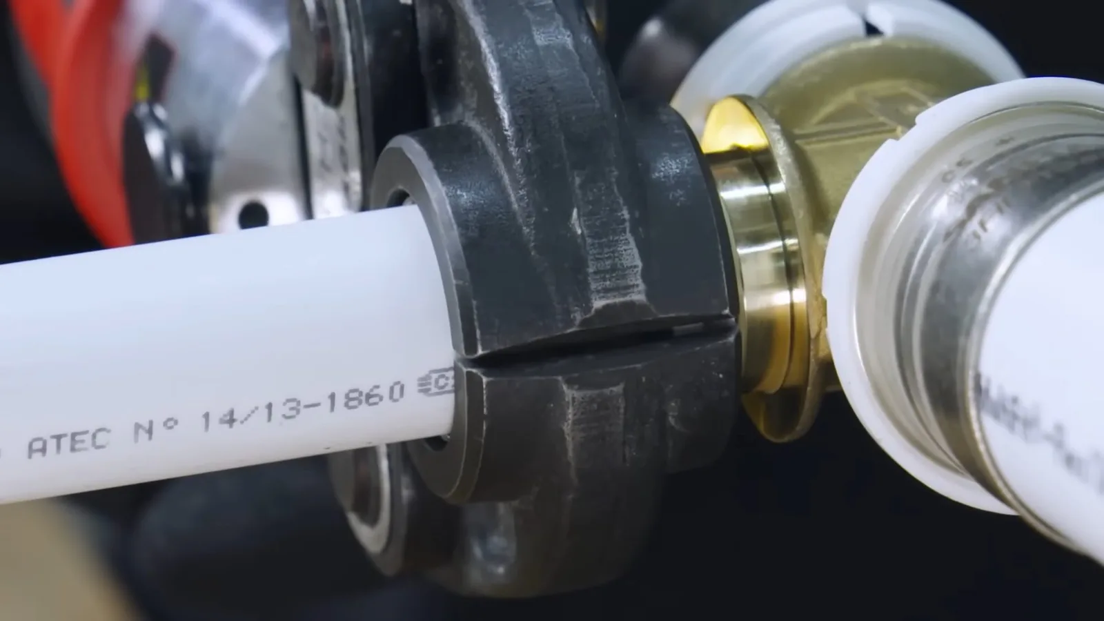 Close view of white plastic pipe with printed markings, a black press collar and a brass fitting beside a white plastic coupling