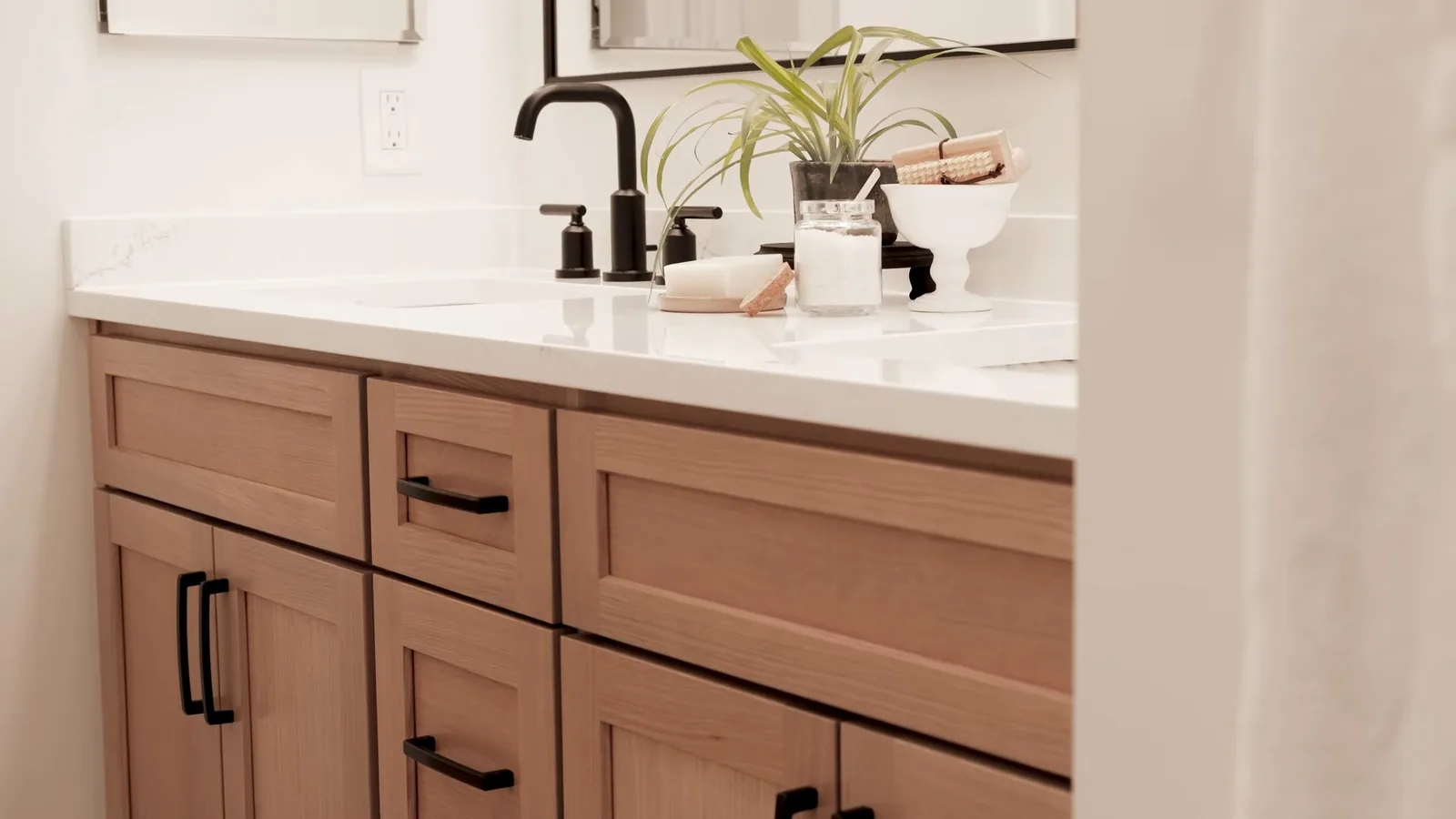 Wood-grain bathroom vanity with a white countertop, black faucet and a small plant, after a remodel