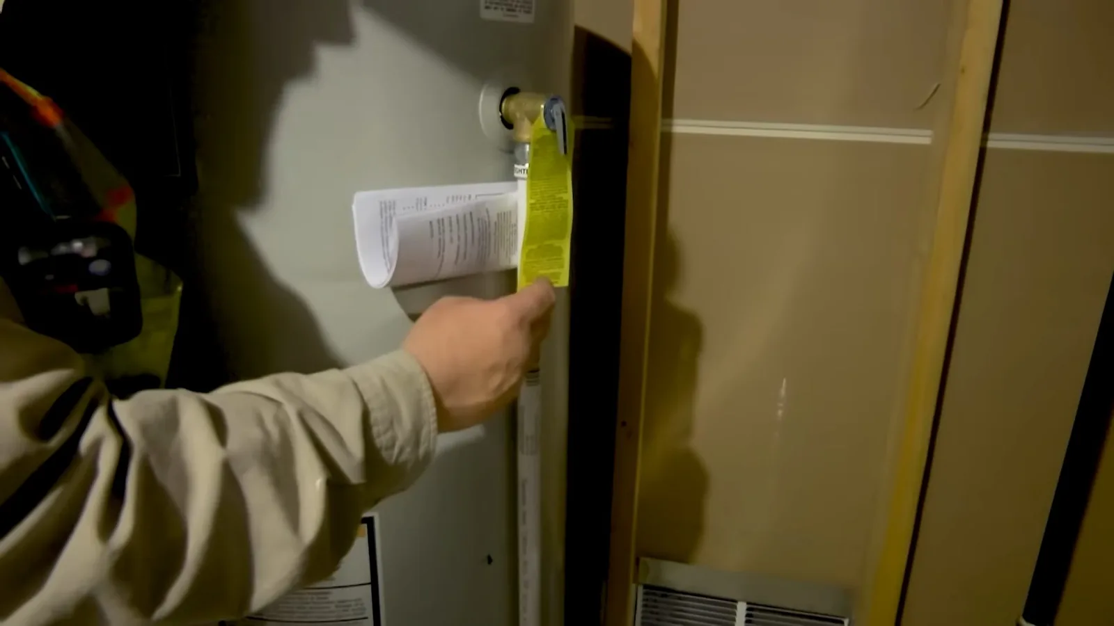 Worker in a khaki shirt holding paperwork and checking the front panel of a gas water heater